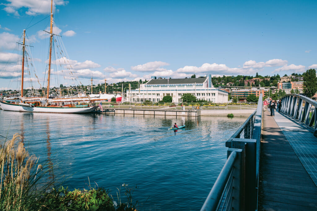 A view of South Lake Union featuring tall ships and MOHAI with a pedestrian bridge extending away from the viewer at the right.