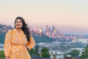 Woman smiling at the camera in front of the Seattle skyline at sunset from Ella Bailey Park in Magnolia
