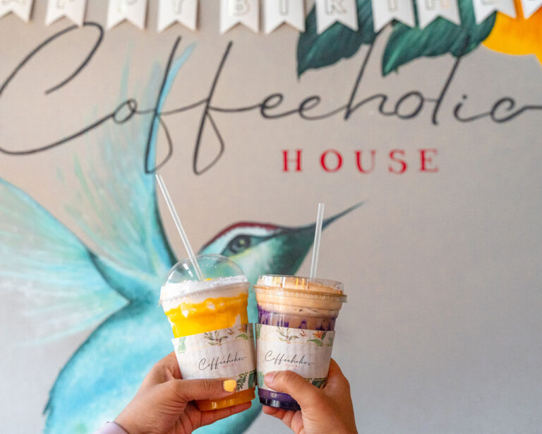 two drinks held up in front of a bird mural at Coffeeholic House