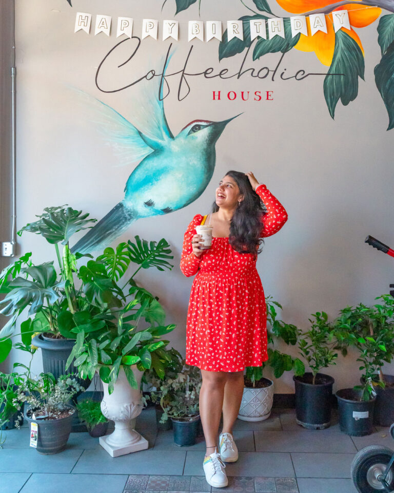 a woman posing with her coffee drink in front of a bird mural at Coffeeholic House