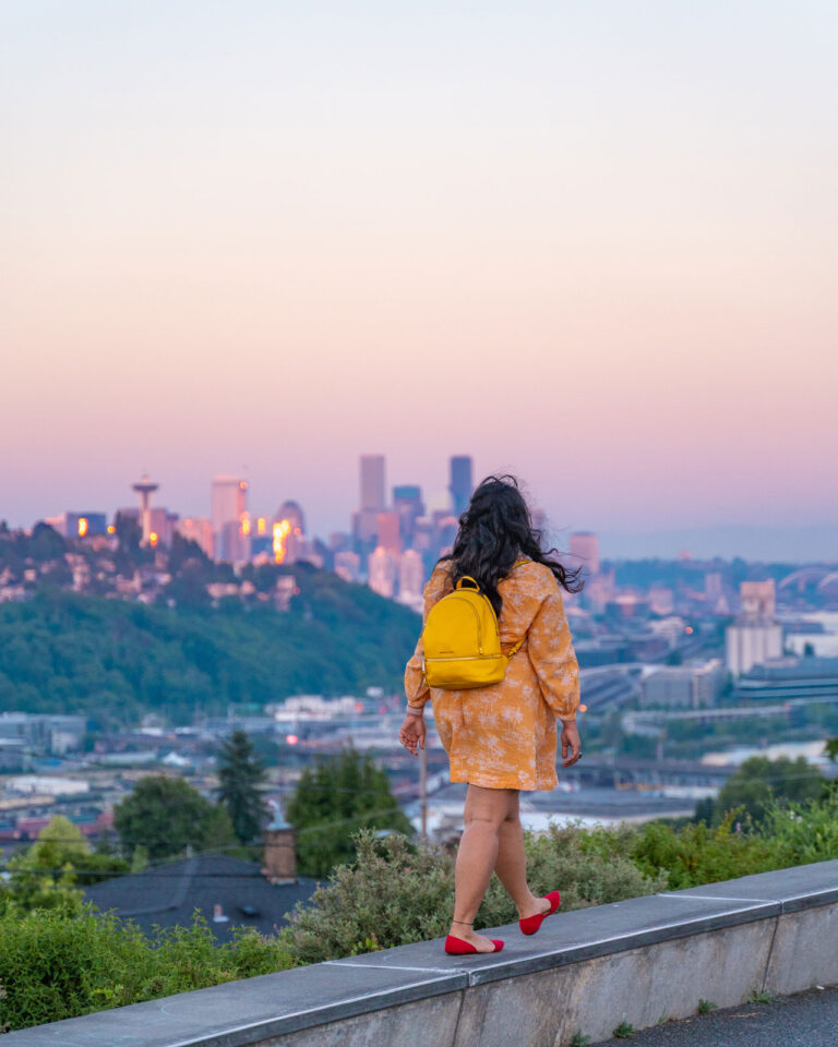 Woman walking in front of the Seattle skyline at sunset from Ella Bailey Park in Magnolia