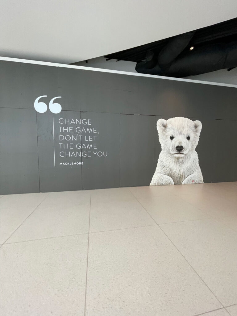 A wall features a mural of a white bear cub next to a quote by Macklemore: "Change the game, don't let the game change you." The background is dark gray, and the floor is light-colored tile.
