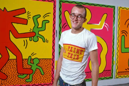 Artist Keith Haring wears a white t-shirt with a yellow rectangle in the middle that reads 