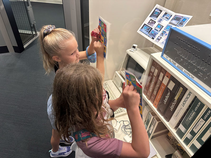 Two young girls mark off their scavenger hunt sheets after finding A LEGO computer hidden in the Microsoft display at MOHAI.