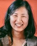 A person with long dark hair is smiling at the camera against an orange background.
