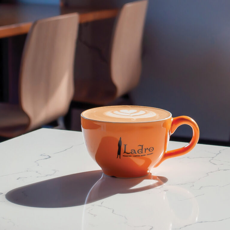 An orange Caffe Ladro cup full of coffee sits on a polished grey surface.