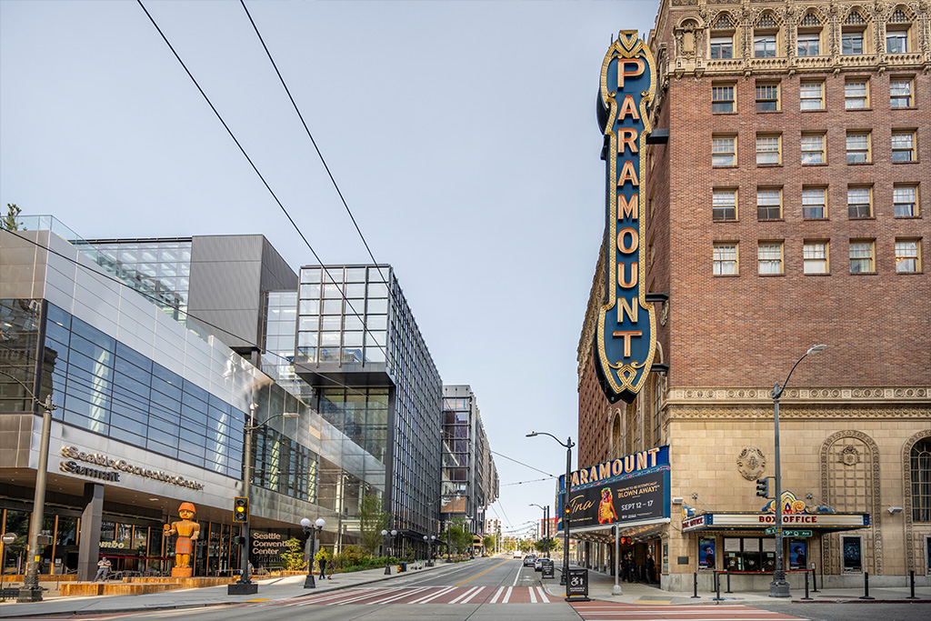 A photo of the brick exterior of Paramount Theatre with the large marquee sign on the left. The theatre is across the street from the Seattle Convention Center Summit building.