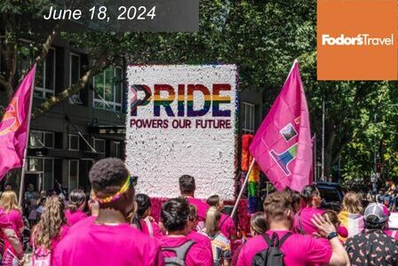 People walk down street in Pride Parade with a large float that reads 