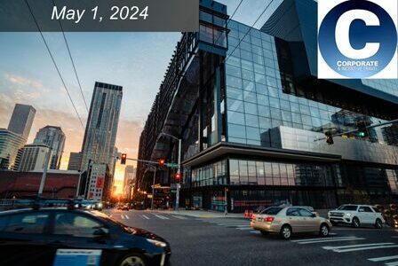Cars pass by a glass building in downtown Seattle as the sun sets in the background.