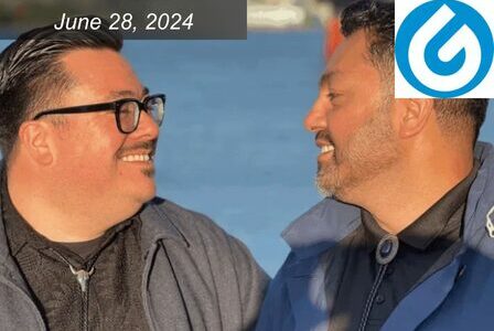 Two men smile at each other with a view of the ocean behind them