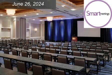 A room of tables and chairs facing a screen and stage in a Grand Ballroom at Seattle Marriott Waterfront