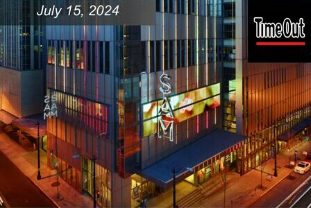 Exterior of a modern building at night, lit up with red lights and sign that reads 