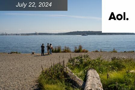 Three people stand on the shore of Elliott Bay at Golden Gardens on a sunny day.