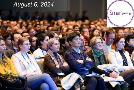 A large audience attentively listens at a conference. The date 