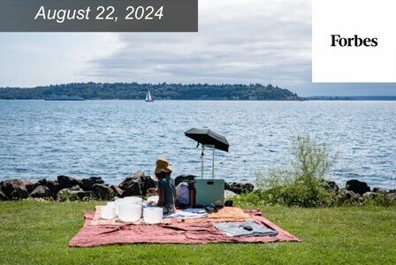 Woman sitting on a picnic blanket overlooking a lake.