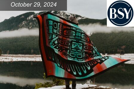 A person stands outdoors in winter, wrapped in a colorful blanket with abstract designs.