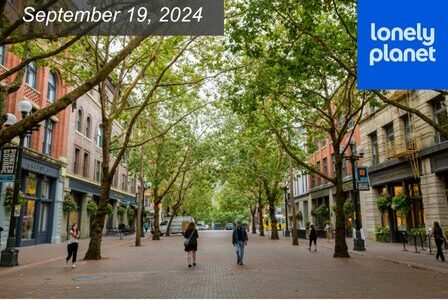 A tree-lined street in a city with brick-paved sidewalks. People are walking among historic buildings in Pioneer Square, Seattle.