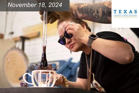 A person wearing sunglasses is shaping molten glass with tools in a workshop.