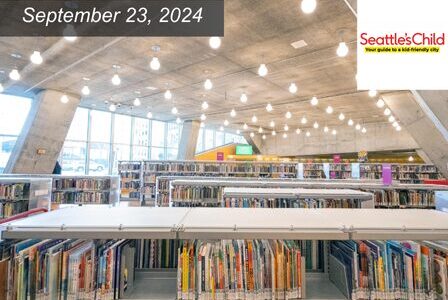 A modern library interior with tall shelves filled with books, illuminated by rows of hanging lights.