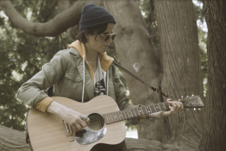 A woman sitting on a tree playing a guitar.