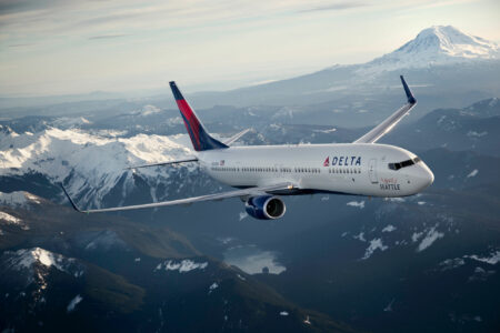A photo of a white airplane flying in the sky over mountains. Mount Rainier is in the back right corner.