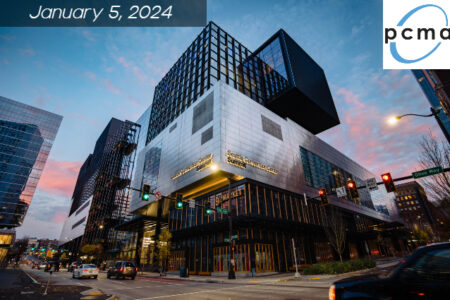 Modern city street scene featuring a large, contemporary building under evening sky. Signage displays 