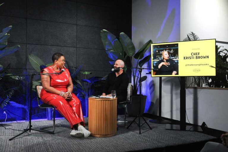Black female Chef Kristi Brown sits on stage with white male podcast host Mike Schibel