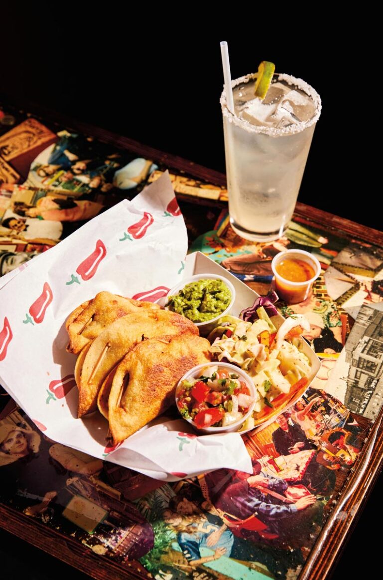 A plate of crispy tacos with guacamole, salsa, and sauce on the side, accompanied by a margarita with a salted rim and lime wedge. This delicious setup graces an artistic tabletop, embodying the vibrant spirit of Seattle's Ballard neighborhood.