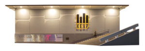 A photo illustration depicting a grey building with a yellow and black sign near the mid-right.