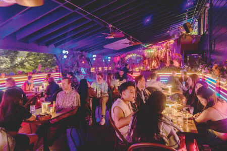 A photo of people eating and drinking at tables and the bar at Carnelian Bay. Purple and pink lights fill the space.