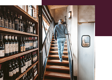 A man walking up the stairs near a shelf of wine at Terra Plata